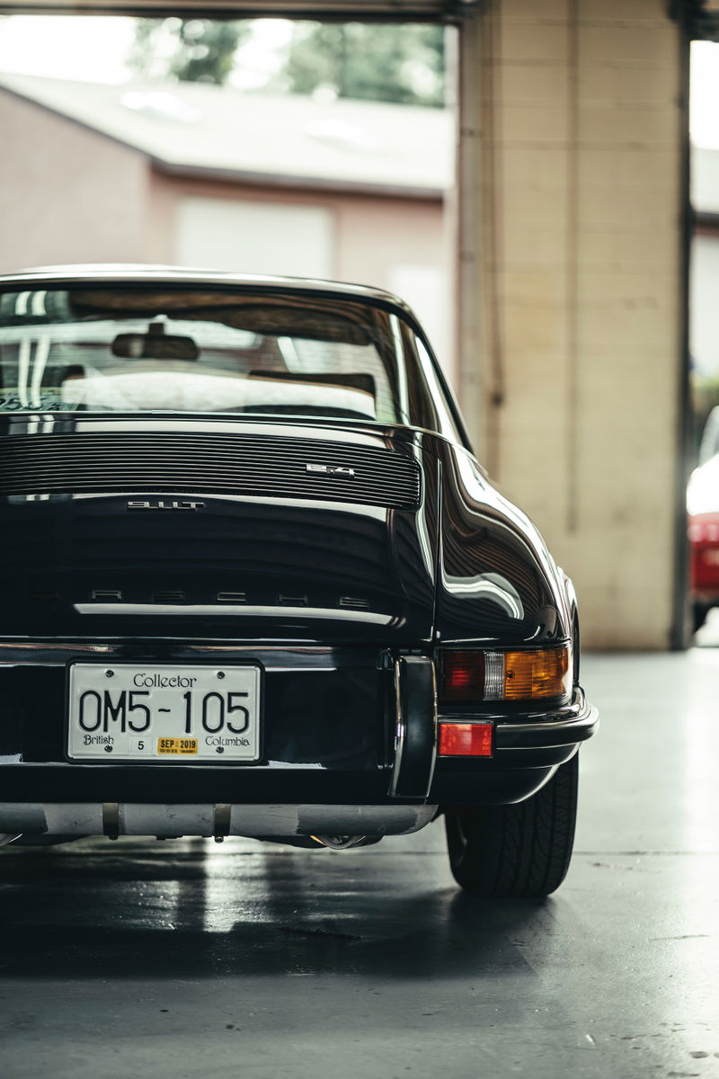 Rear view of a black classic Porsche 911T sports car. Features horizontal decklid grille, chrome bumper trim, and Collector plate.