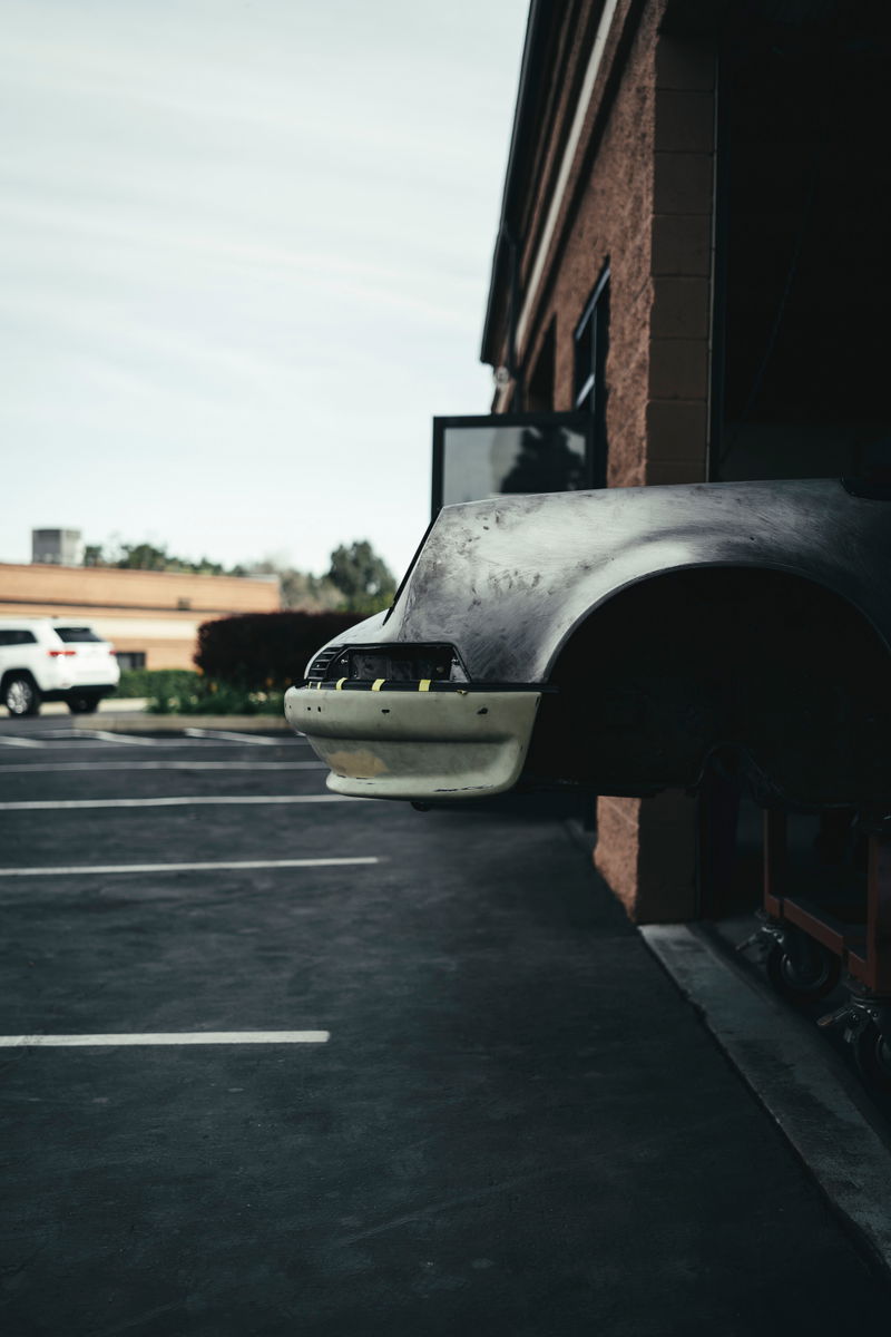 Air-cooled Porsche 911 front fender and bumper in bare metal and primer, undergoing custom restoration bodywork.