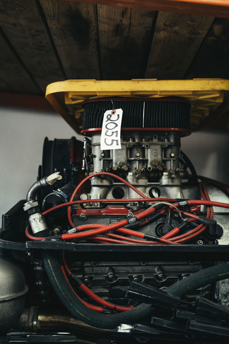 Close-up of a classic performance engine, featuring multiple side-draft carburetors, red ignition wires, and a black open-element air filter.