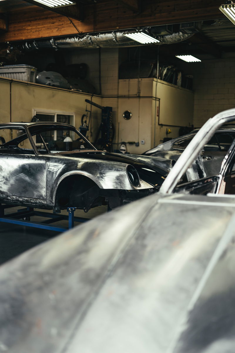 Bare metal classic Porsche 911 body, prepped for restoration or custom paint, on a jig in a Los Angeles workshop.