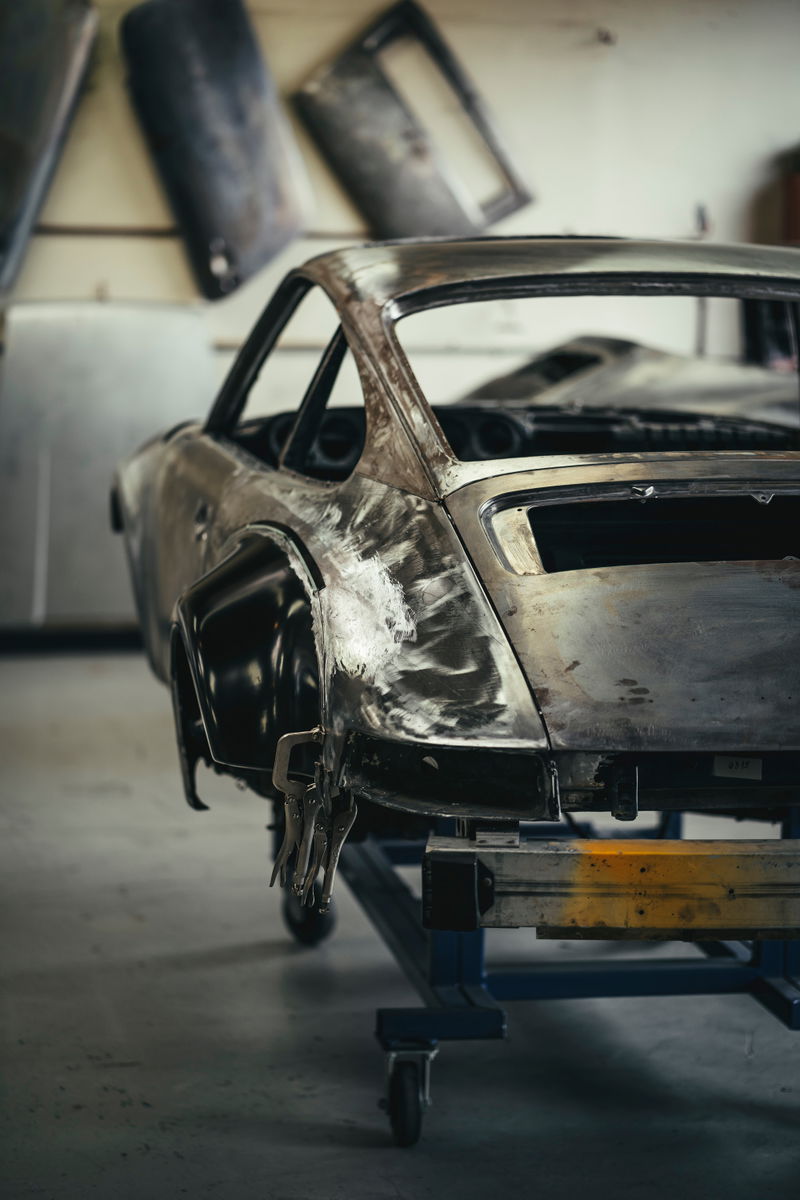 Classic Porsche 911 custom widebody build, bare metal shell on a chassis jig with RSR fender flares clamped.