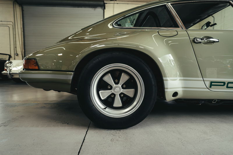 Classic light green Porsche 911 rear quarter, with white PORSCHE livery stripes, chrome door handle, and polished Fuchs wheels.