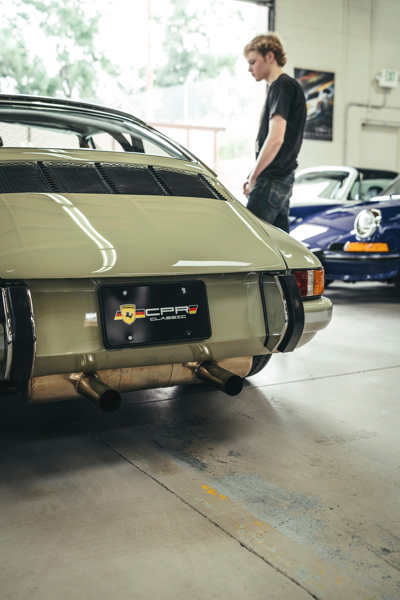 Sage green early Porsche 911 Targa rear, showing engine lid grilles, bumperettes, heat-wrapped dual exhaust, and CPR Classic plate.