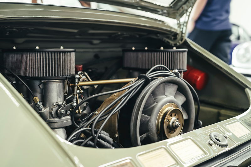 Muted green classic Porsche 911 air-cooled flat-six engine, showing dual air filters, carburetors, and cooling fan.