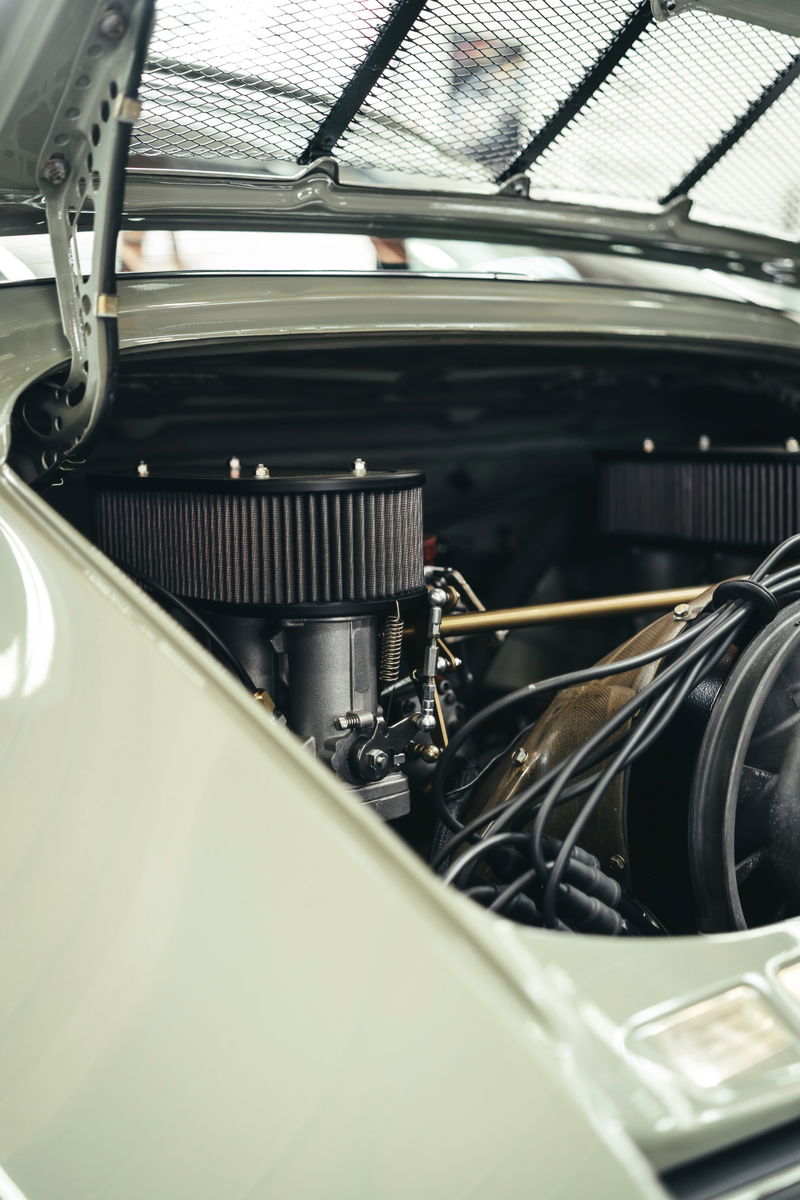 Close-up: Light green vintage Porsche 911's air-cooled flat-six engine. Dual filters, carbs & ignition wires visible under mesh grille.