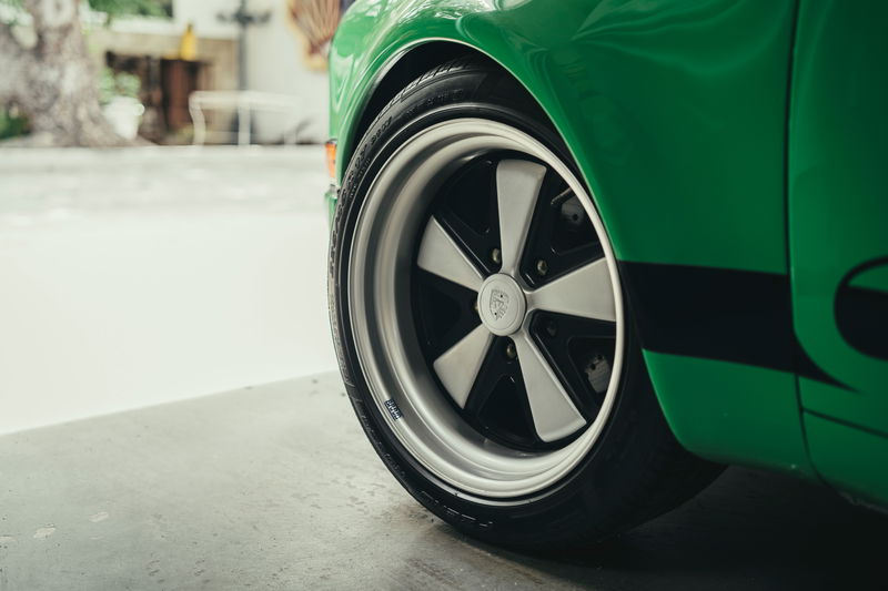 Close-up of a green Porsche 911's Fuchs-style alloy rims and tire, featuring a black side livery on the fender.