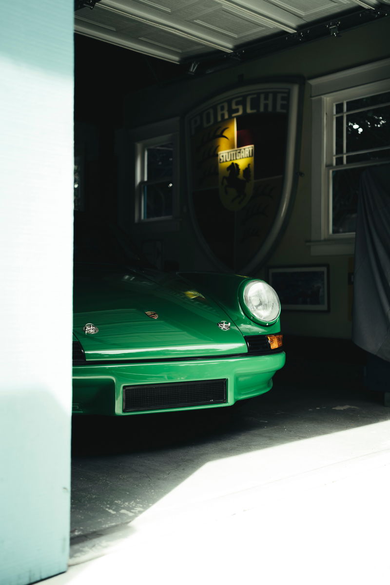 Vivid green vintage Porsche 911 peeks from garage, showcasing its signature round headlight, streamlined front bumper, and grille.