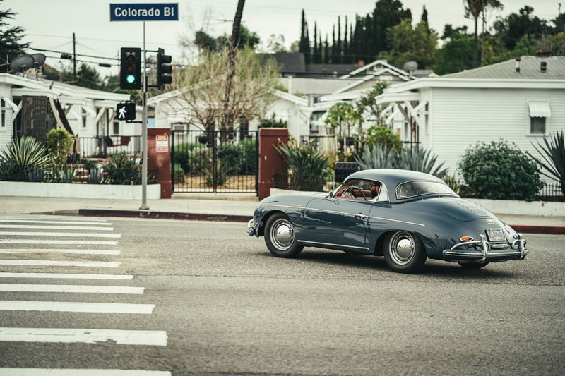 Vintage slate blue Porsche 356 Coupe, featuring chrome trim and full-disk hubcaps, drives on Colorado Blvd, Los Angeles.