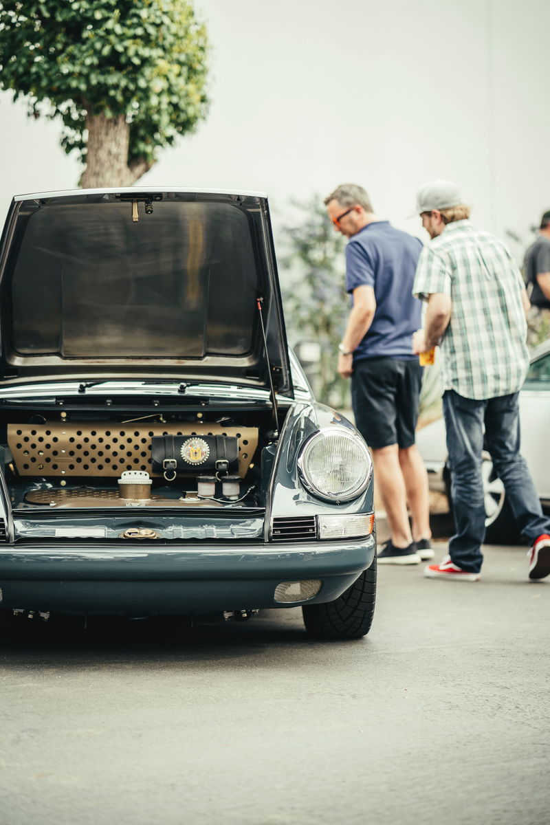 Slate Grey classic Porsche 911, frunk open revealing custom tan perforated panel, leather trim & accessories at a car show.
