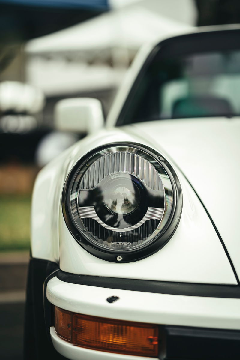 White classic Porsche 911's modern LED headlight with fluted lens, amber turn signal, and black bumper trim.