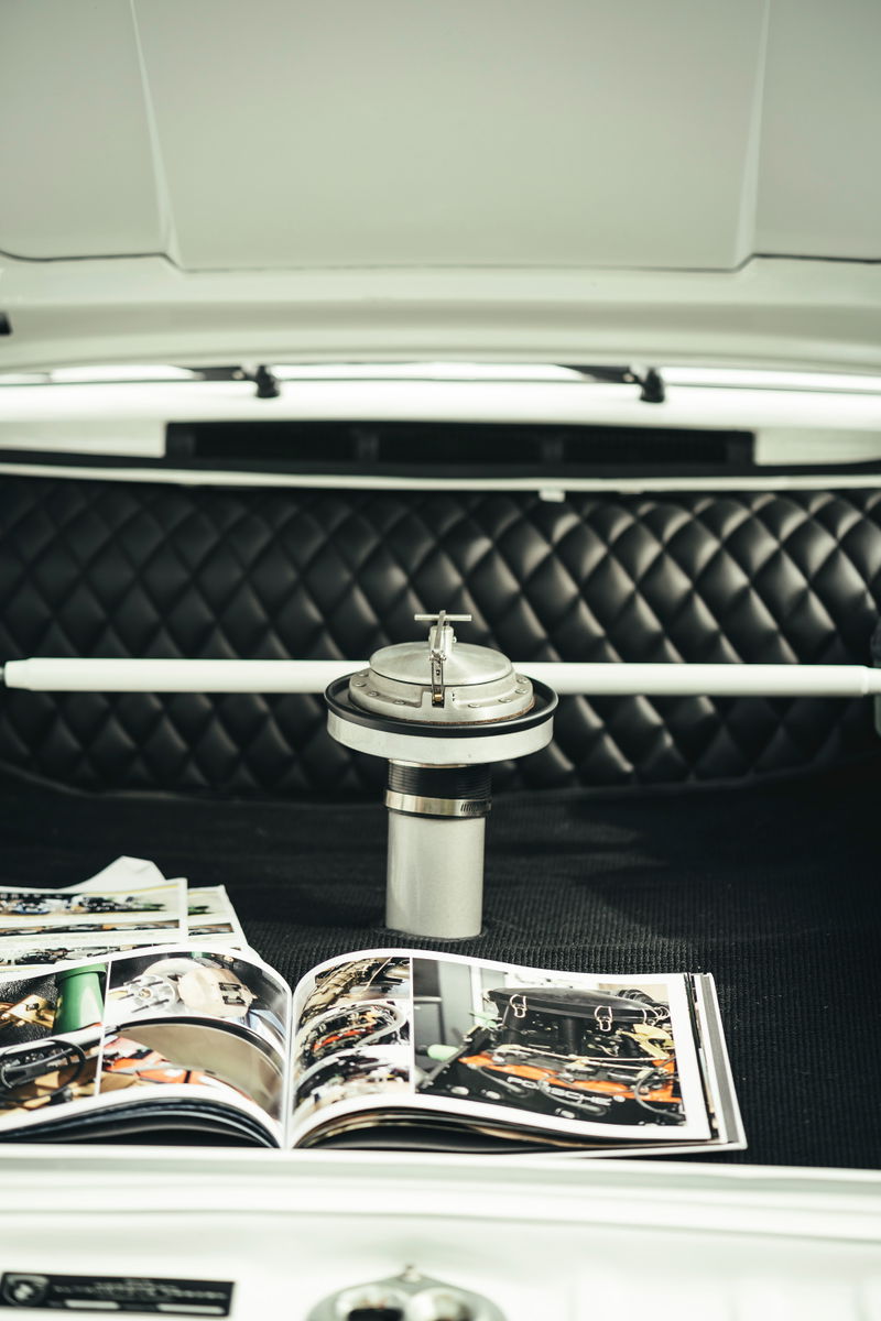 White air-cooled Porsche interior: vintage aluminum race fuel filler, quilted black leather bulkhead, and white strut bar.