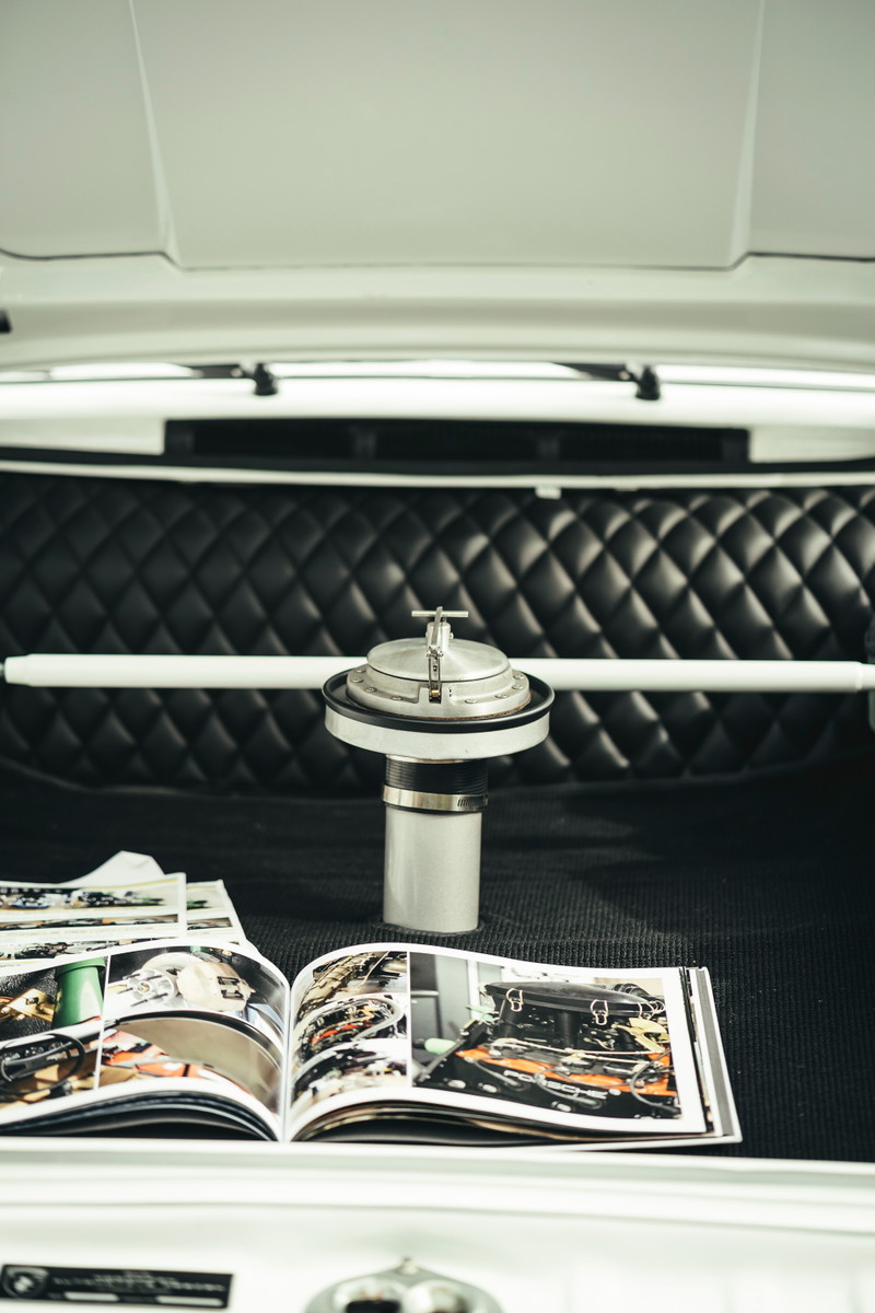 White air-cooled Porsche interior: vintage aluminum race fuel filler, quilted black leather bulkhead, and white strut bar.