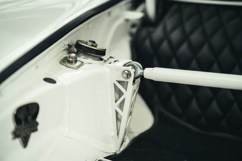 White Porsche 911 (air-cooled) strut tower with custom lightweight strut bar, spherical bearing mount. Black quilted interior.