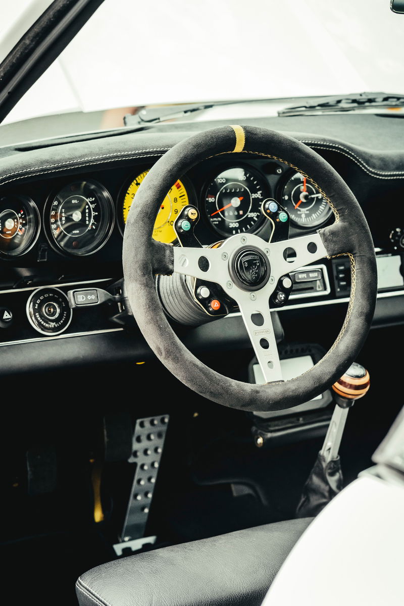 Singer 911 interior: Alcantara steering wheel with yellow stripe, bespoke yellow gauges, wood shift knob, and drilled pedals.