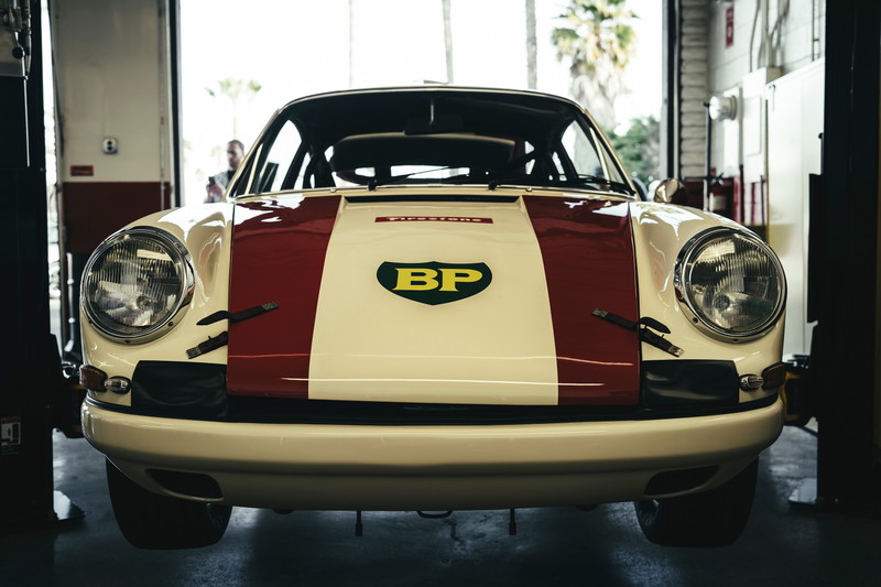 Vintage air-cooled Porsche 911 race car, white with red stripe & BP livery. Front fascia, classic headlights, and hood pins.