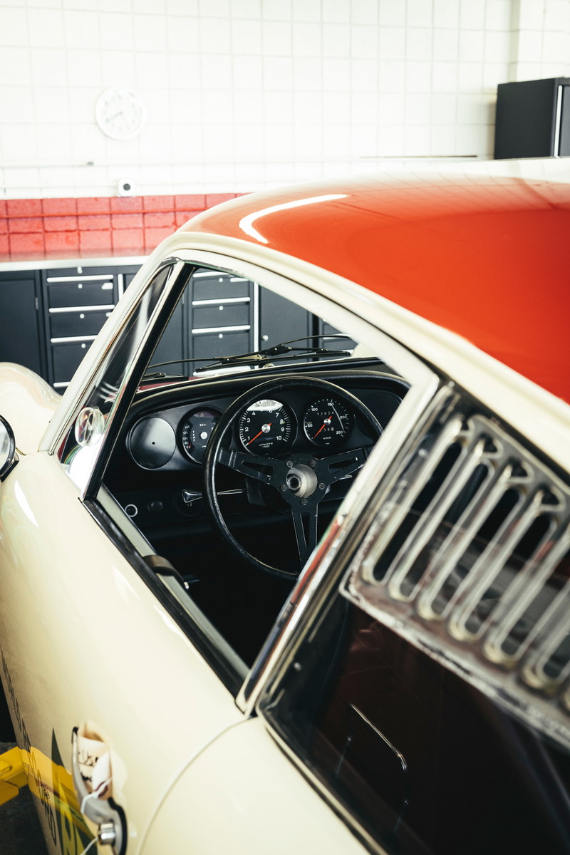 Classic Porsche 911 with two-tone red & cream livery. View of the vintage interior with 3-spoke steering wheel and louvered quarter window.