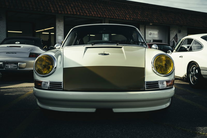 Front view of custom cream air-cooled Porsche 911 with olive stripe livery, yellow headlights, and integrated front valance.