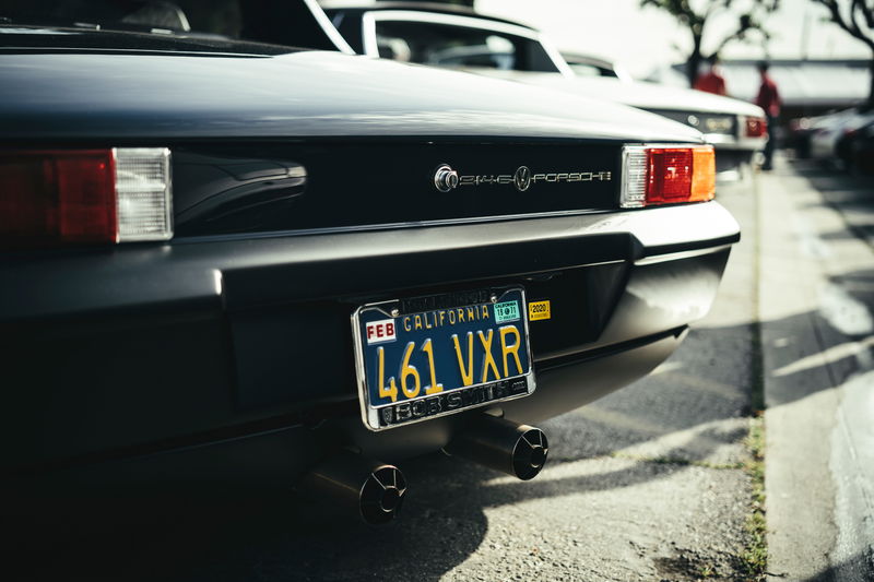 Close-up of a black VW-Porsche 914 rear, 'VW-Porsche' badging, rectangular taillights, CA plate & dual black exhaust tips.