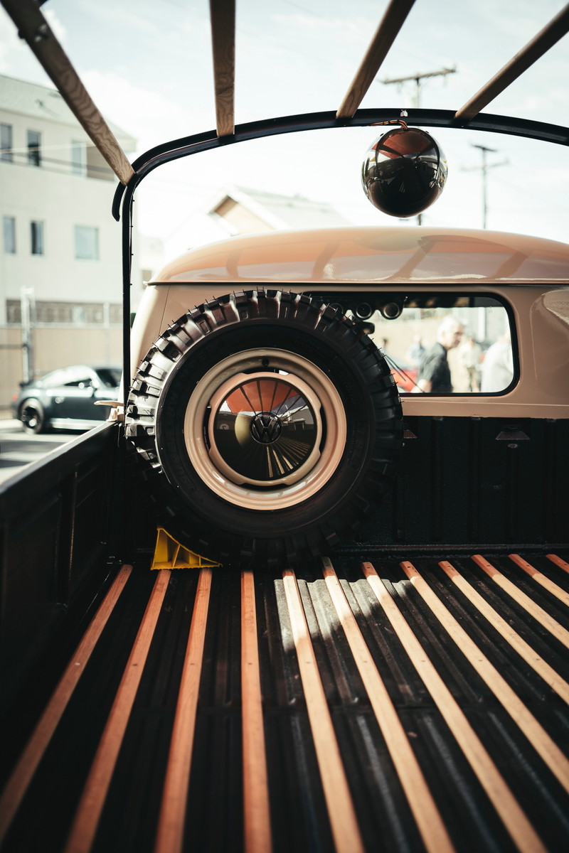 Vintage beige VW Type 2 Single Cab pickup bed, featuring a spare tire with VW hubcap, steel rim, and wood slats. Lit Show LA.