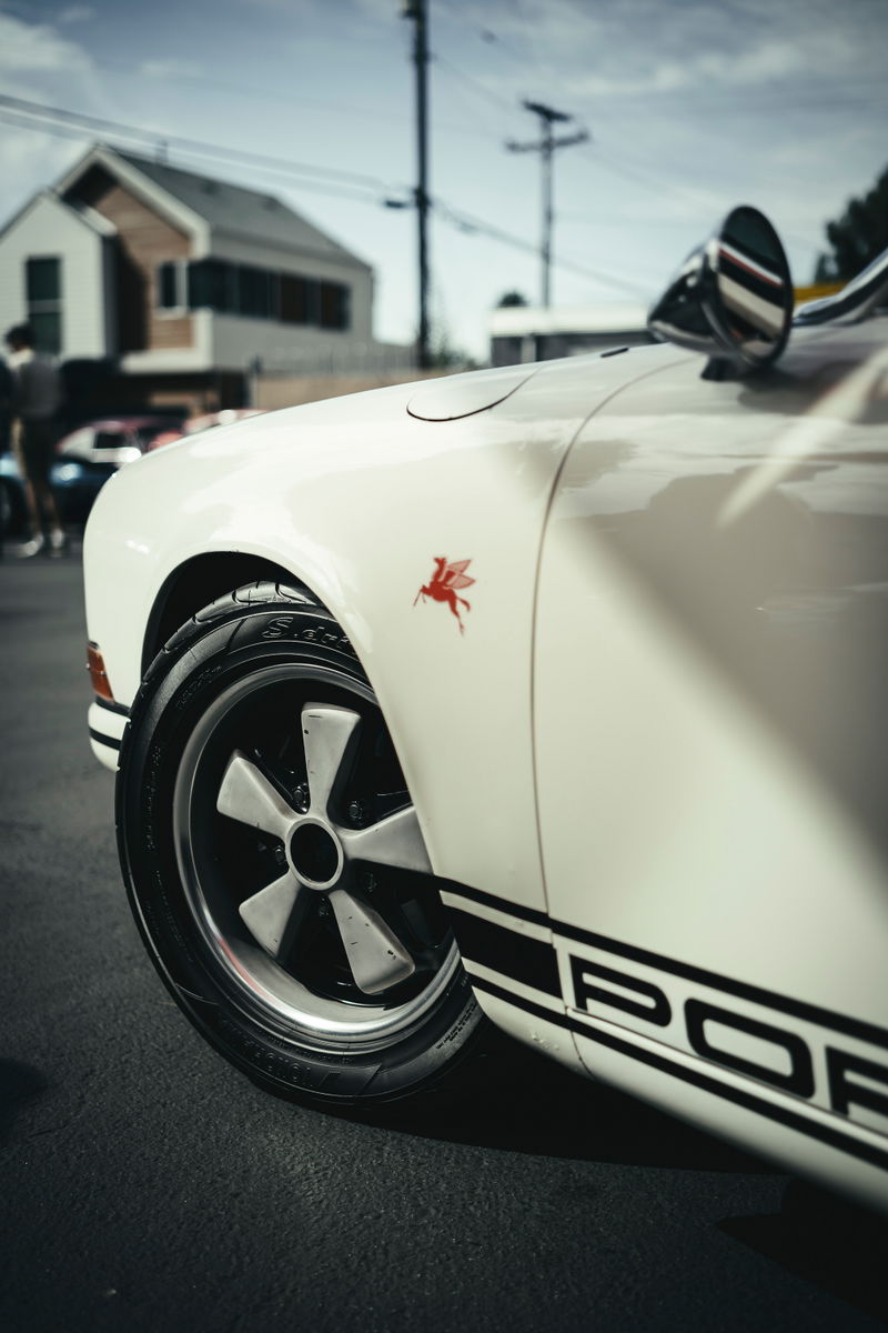 White classic Porsche 911 with iconic Fuchs wheels, red Mobil Pegasus fender badge, and black PORSCHE side livery.