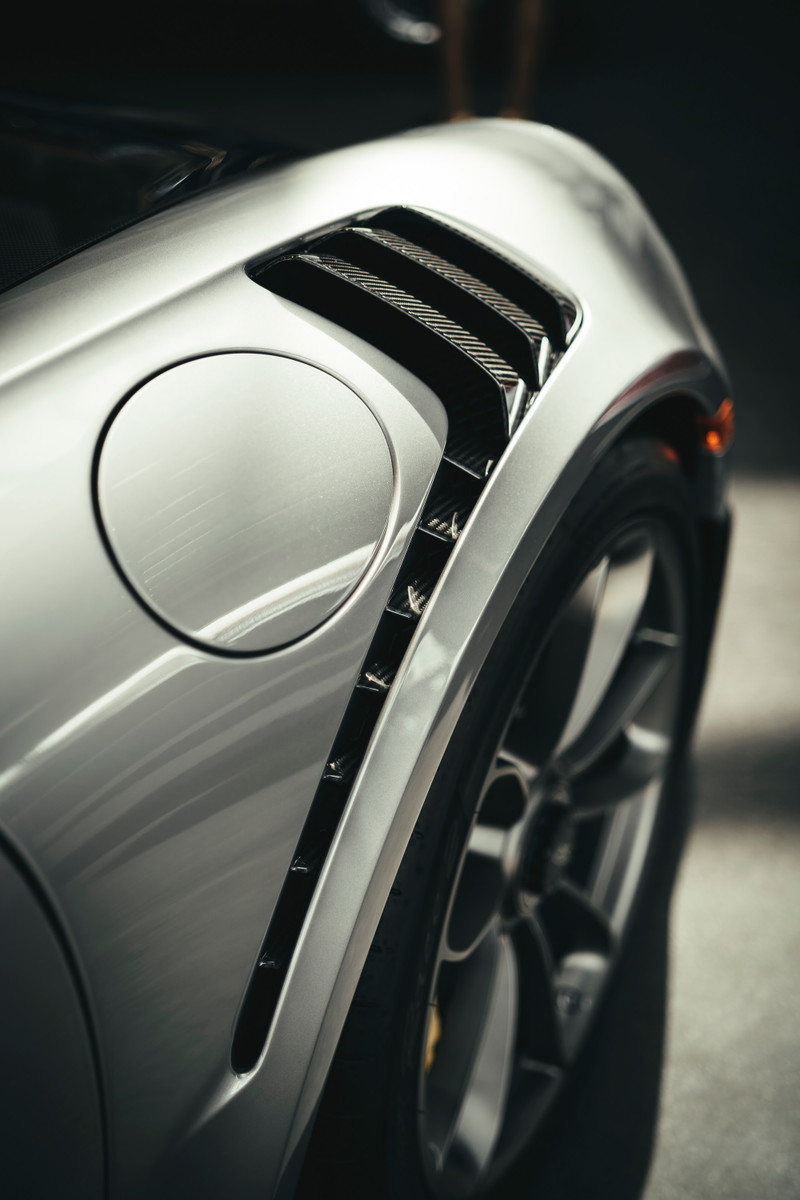 Close-up of a silver Porsche 911 GT3 RS (991.2) rear quarter panel, featuring carbon fiber fender vents, fuel filler, and alloy wheel.