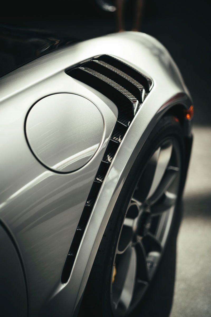 Close-up of a silver Porsche 911 GT3 RS (991.2) rear quarter panel, featuring carbon fiber fender vents, fuel filler, and alloy wheel.