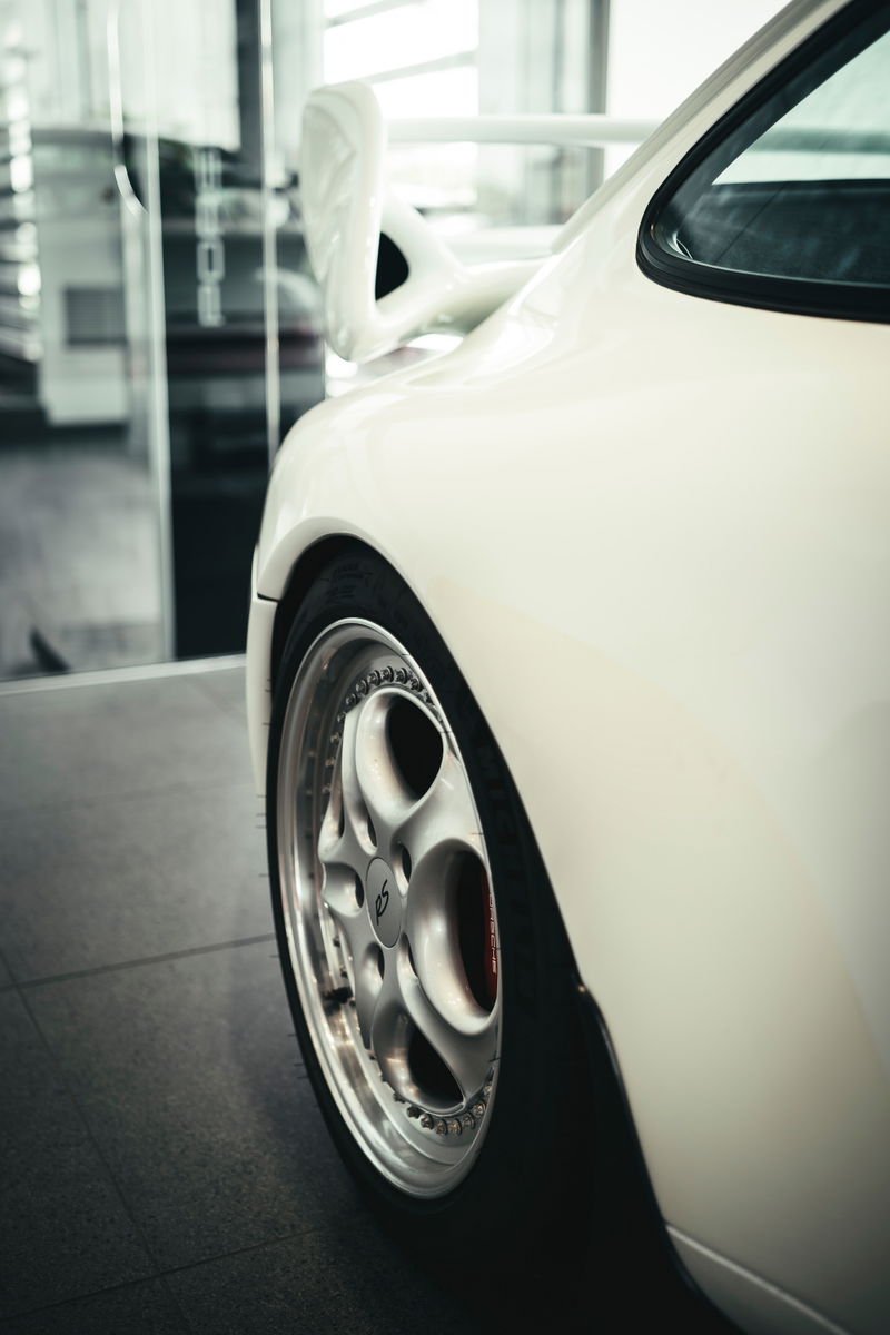 Rear quarter of a white Porsche 993 Carrera RS, showcasing its iconic whale tail wing and multi-piece BBS RS wheels with red calipers.