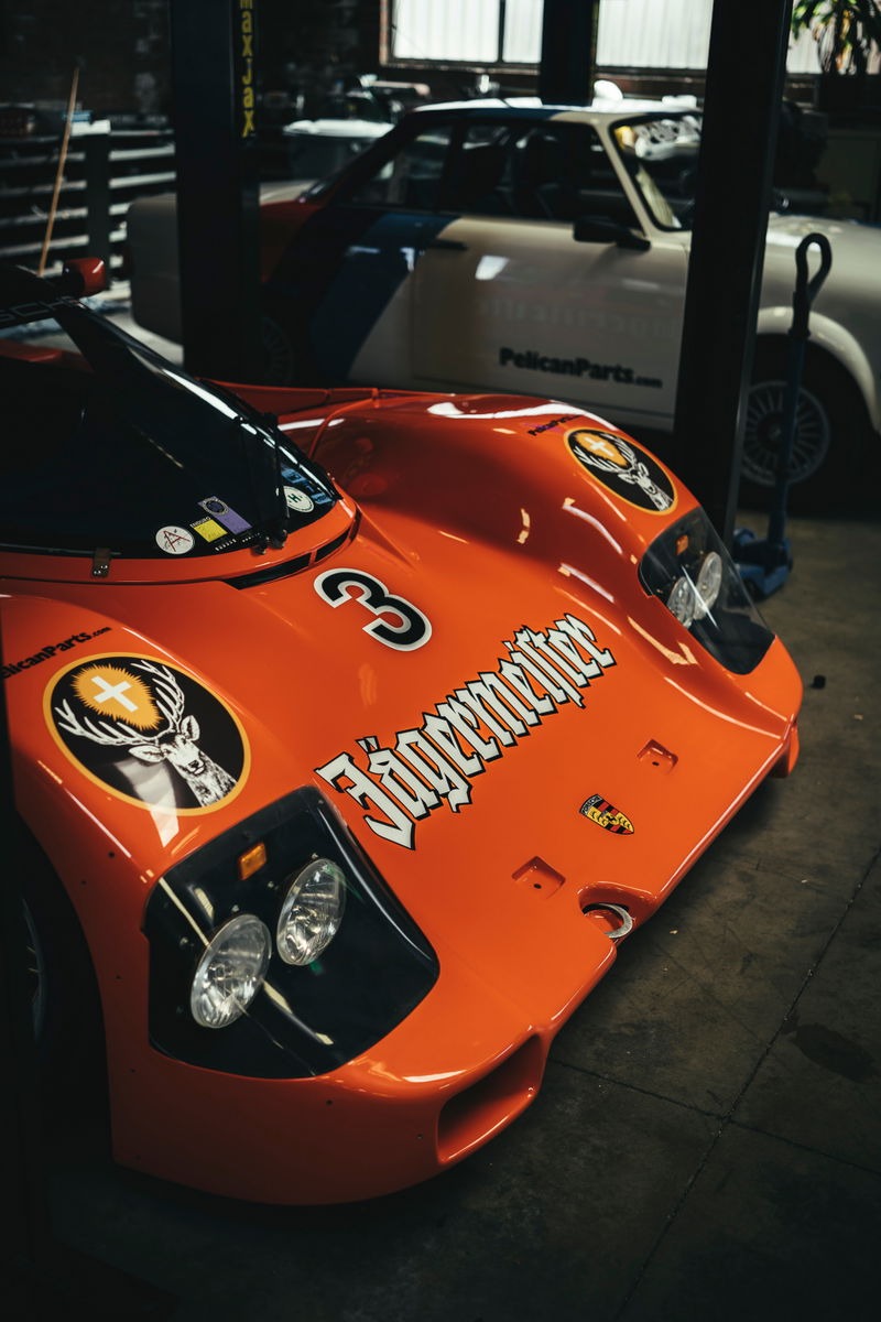 Orange Porsche 962 Group C race car with Jägermeister livery & #3, showcasing its aerodynamic front bodywork & integrated headlights.
