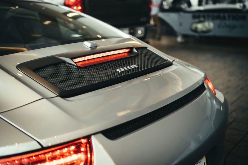 Silver Porsche 992 911 rear view, showcasing its illuminated LED taillight strip, engine cover's mesh grille, and 911 badge.