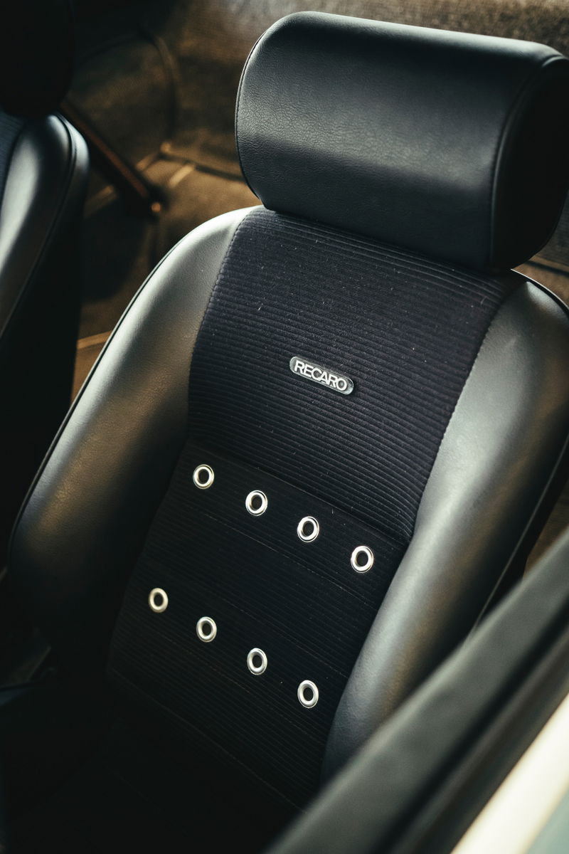 Close-up of a black Recaro sport seat with ribbed fabric and chrome grommets in a classic air-cooled Porsche interior.