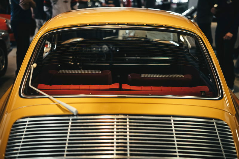 Vintage yellow Porsche 911 rear view showing chrome window trim, engine louvers, and red tartan interior.
