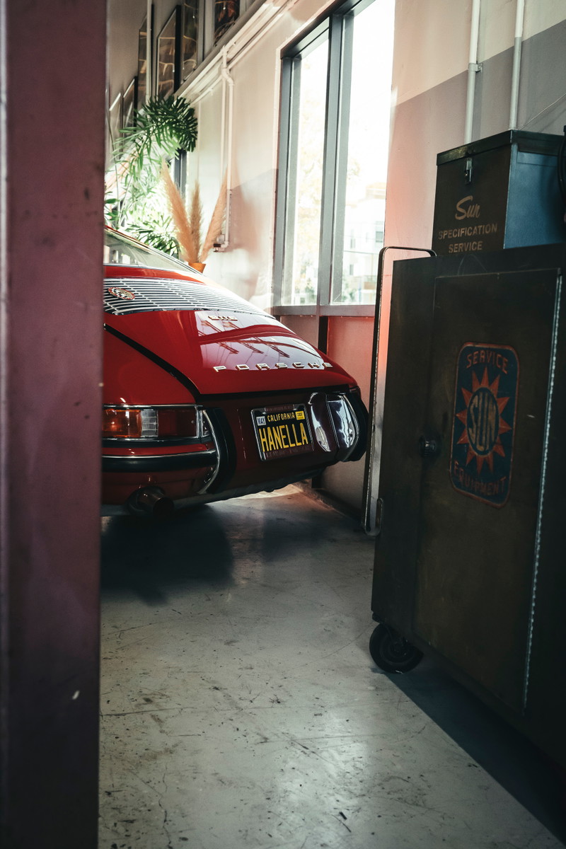Vibrant red classic air-cooled Porsche 911 rear, featuring engine lid louvers, chrome bumperettes, and California plate.