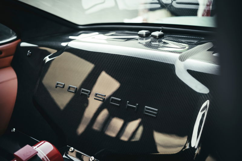 Porsche 911 interior features carbon fiber rear deck with metallic PORSCHE emblem, tan leather trim, and motorsport fire extinguisher.