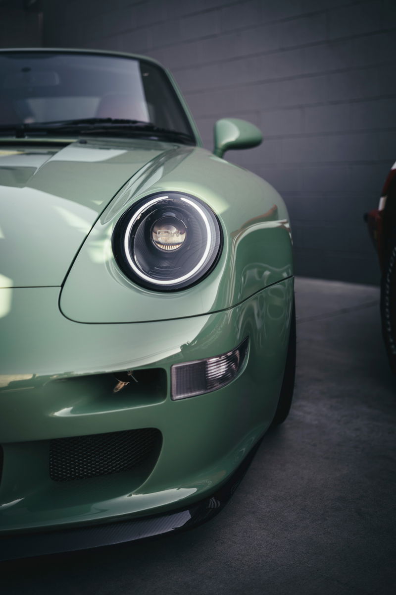 Front fender detail of a mint green Porsche 993 restomod, showcasing custom LED projector headlights & carbon fiber lip.