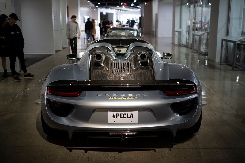 Metallic silver Porsche 918 Spyder rear view, featuring top-exit exhausts, carbon fiber trim, and gold badging. At PECLA.