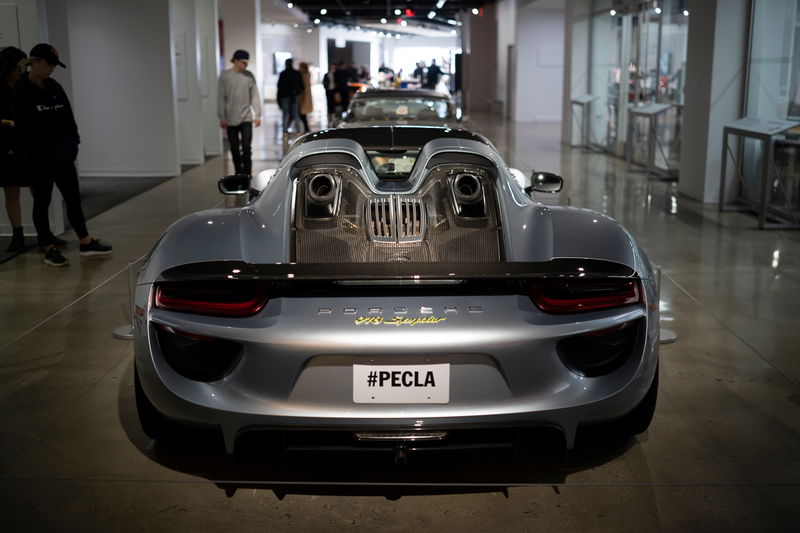 Metallic silver Porsche 918 Spyder rear view, featuring top-exit exhausts, carbon fiber trim, and gold badging. At PECLA.