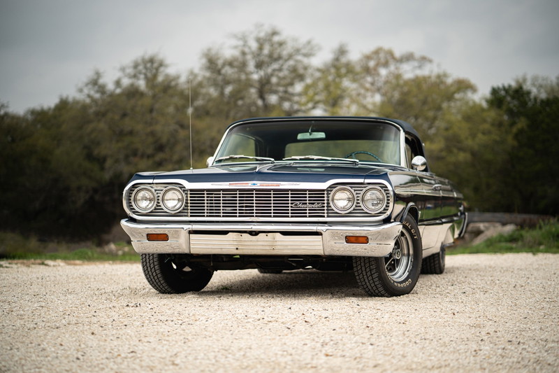 Front view of a dark blue 1964 Chevrolet Impala SS convertible with chrome trim and classic rims.