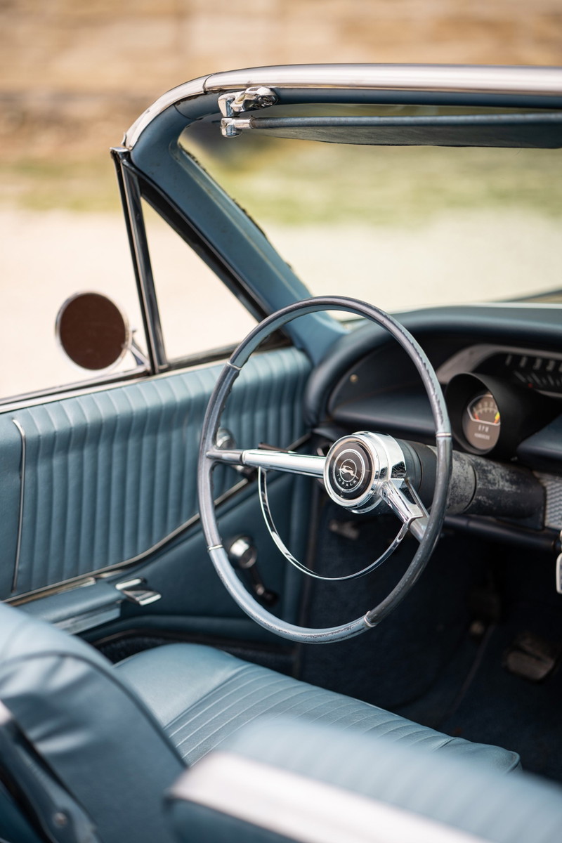 Interior of a 1964 Chevrolet Impala SS convertible, blue vinyl seats, dashboard and steering wheel.