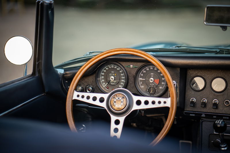 1966 Jaguar E-Type interior: wood-rimmed steering wheel, classic gauges, center console, and door trim.
