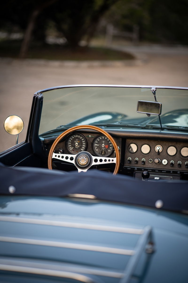 Close-up of a classic 1966 Jaguar XKE dashboard with wood steering wheel and opalescent silver-blue exterior trim.