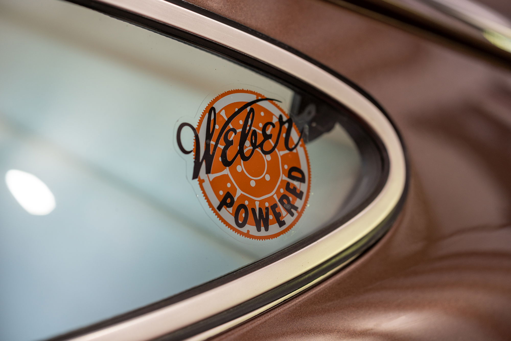 Closeup of a "Weber Powered" decal on the window of a bronze Porsche 911.