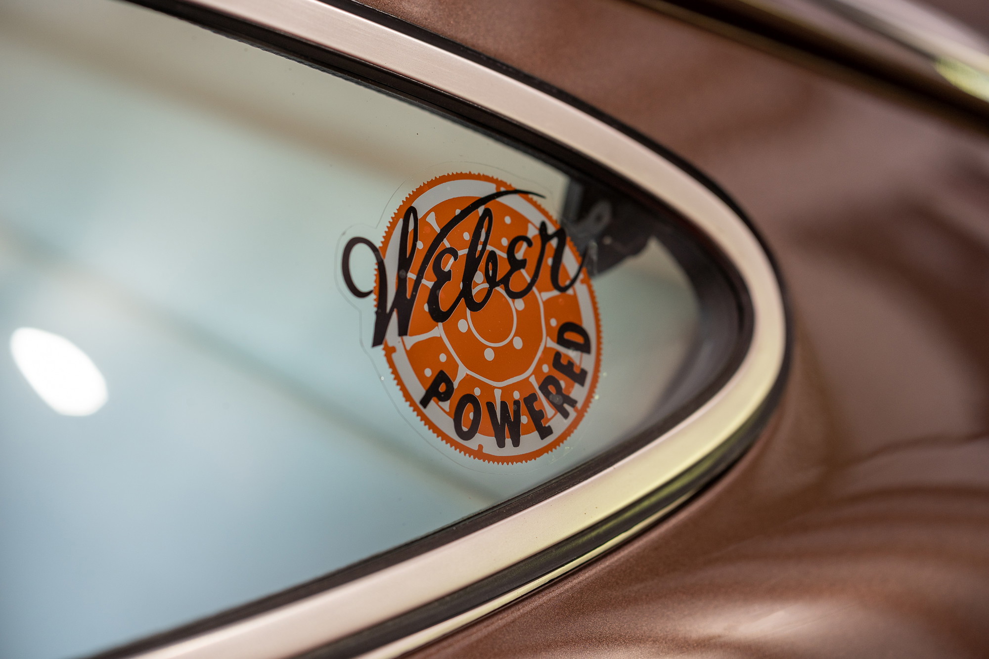 Closeup of a "Weber Powered" decal on the window of a bronze Porsche 911.