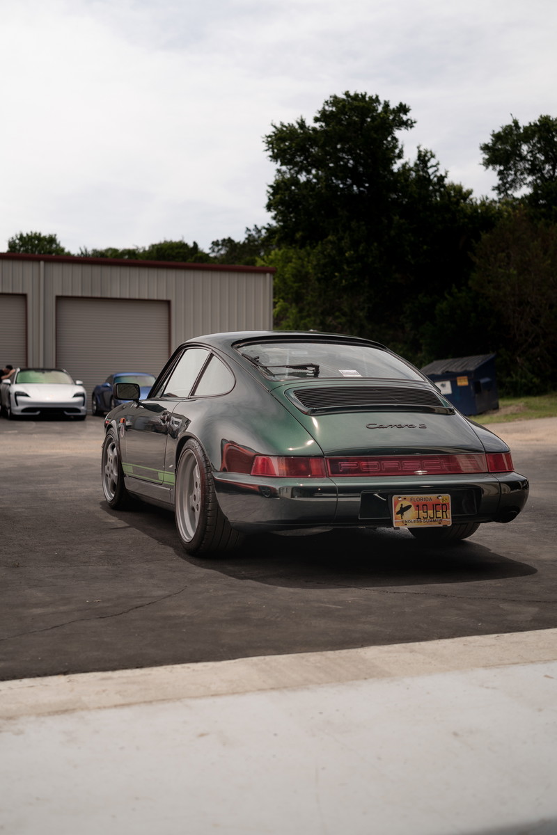 The rear of a dark green Porsche 911 Carrera 2, with silver rims and a green stripe.