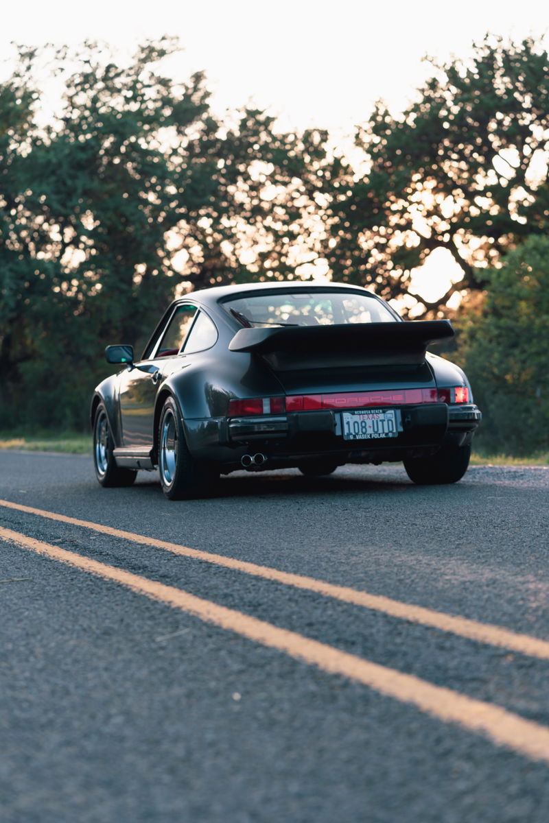 Black 1989 Porsche 930 Turbo Flachbau with whale tail spoiler, polished rims, and dual exhaust.