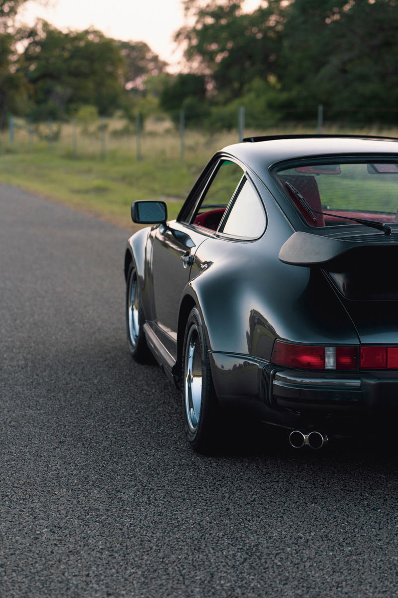 Rear view of a black 1989 Porsche 930 Turbo Flachbau with chrome rims and dual exhaust.