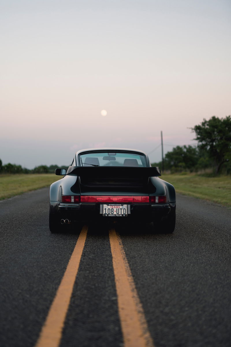 Black 1989 Porsche 930 Turbo Flachbau with whale tail spoiler on a lonely road.