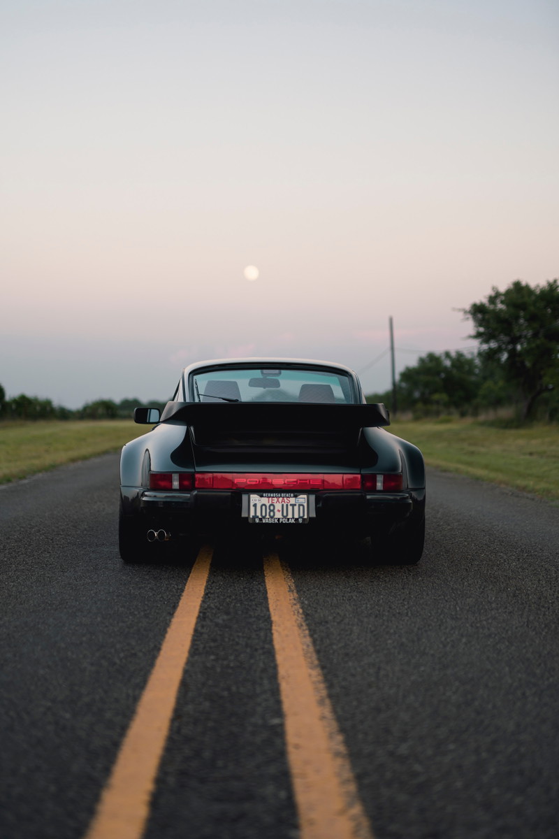 Black 1989 Porsche 930 Turbo Flachbau with whale tail spoiler on a lonely road.