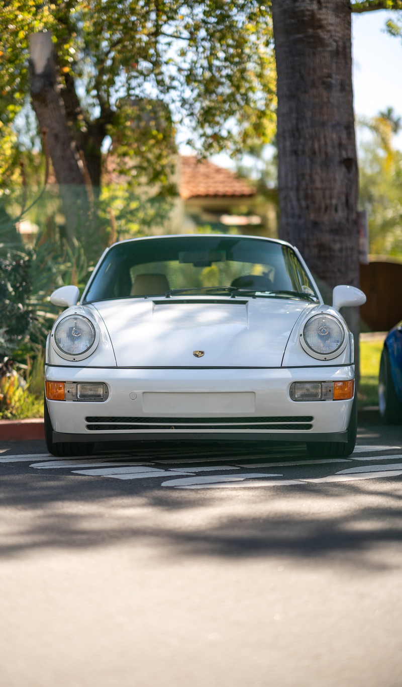White Porsche 911 Carrera 4 (964) parked at a sunny outdoor car show.