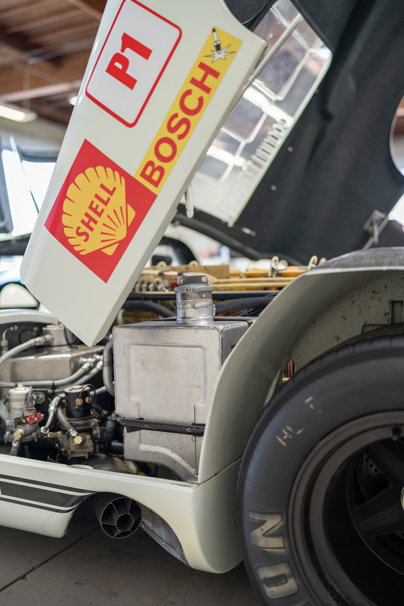 Vintage race car with "P1" and Shell/Bosch livery on open hood. Exposed engine bay, black rims, exhaust visible.