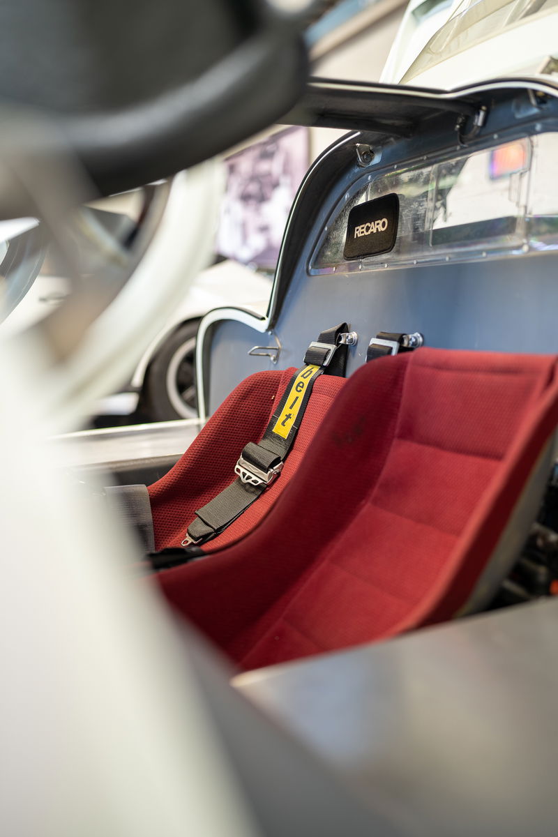 Red Recaro racing seats and harnesses in a silver classic sports car with "RECARO" branding.